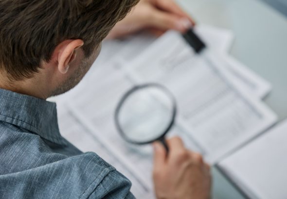businessman-looking-through-magnifying-glass-documents-note-office