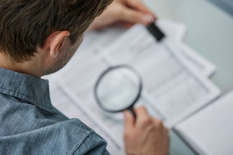 businessman-looking-through-magnifying-glass-documents-note-office